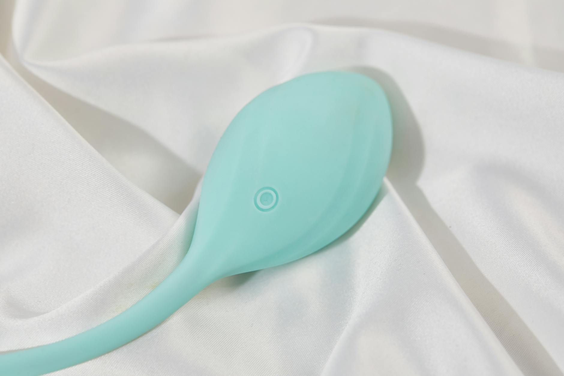 A teal lemon clitoral vibrator on smooth white silk fabric
