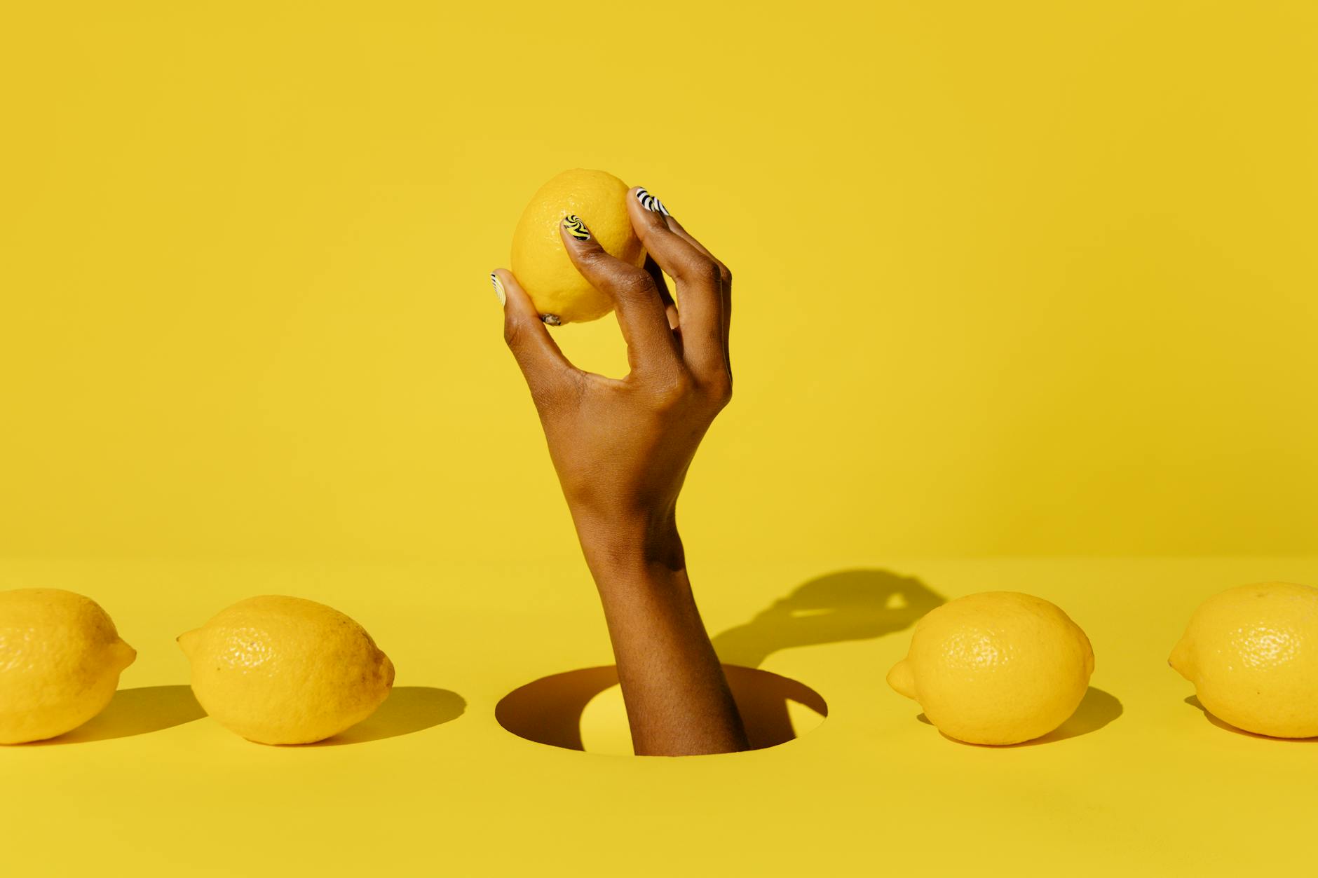 A hand holding a fresh lemon against a bright yellow background, symbolizing zest and vitality in pleasure