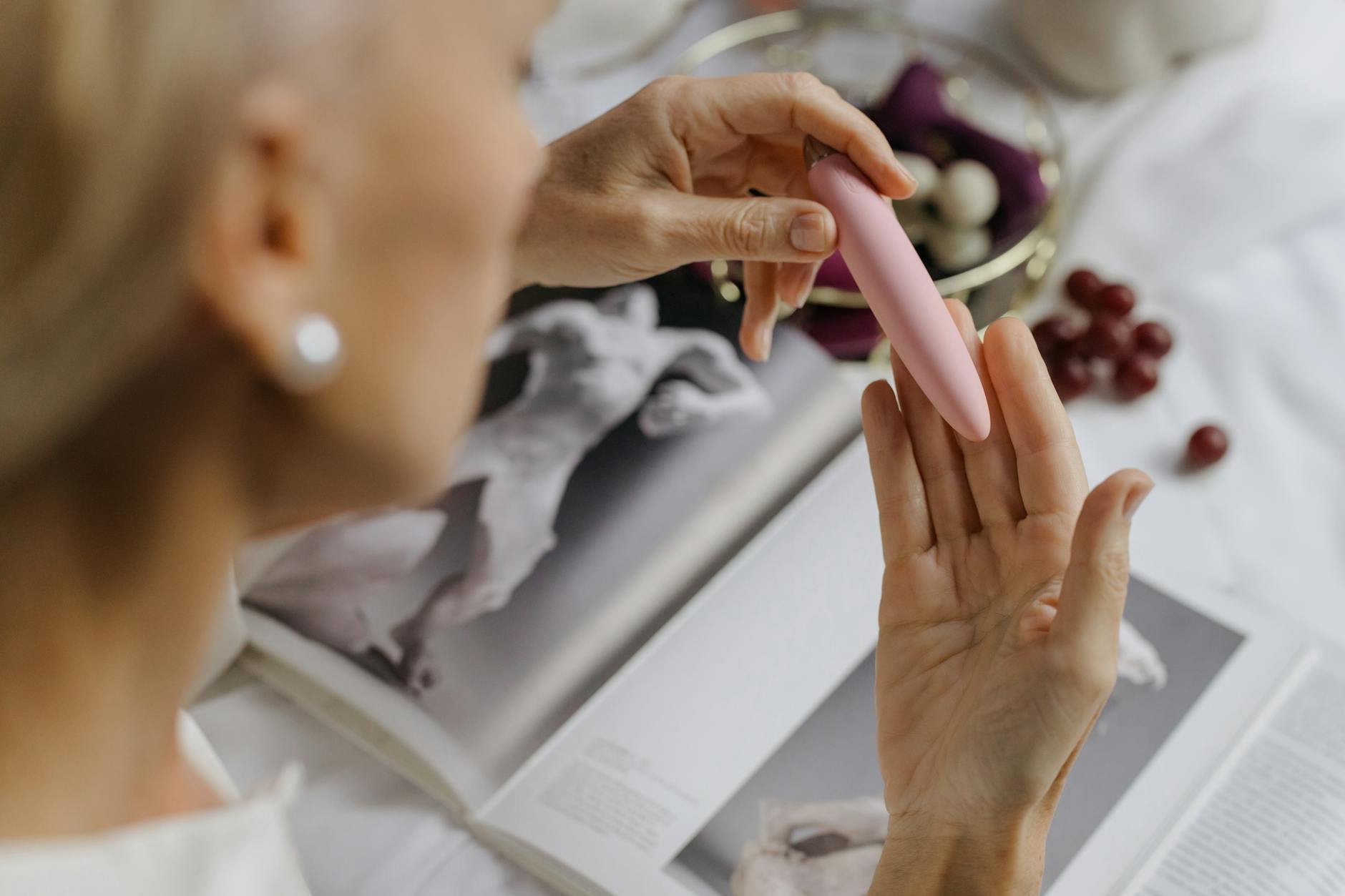 Close-up of a woman holding a pink vibrator with art books in the background