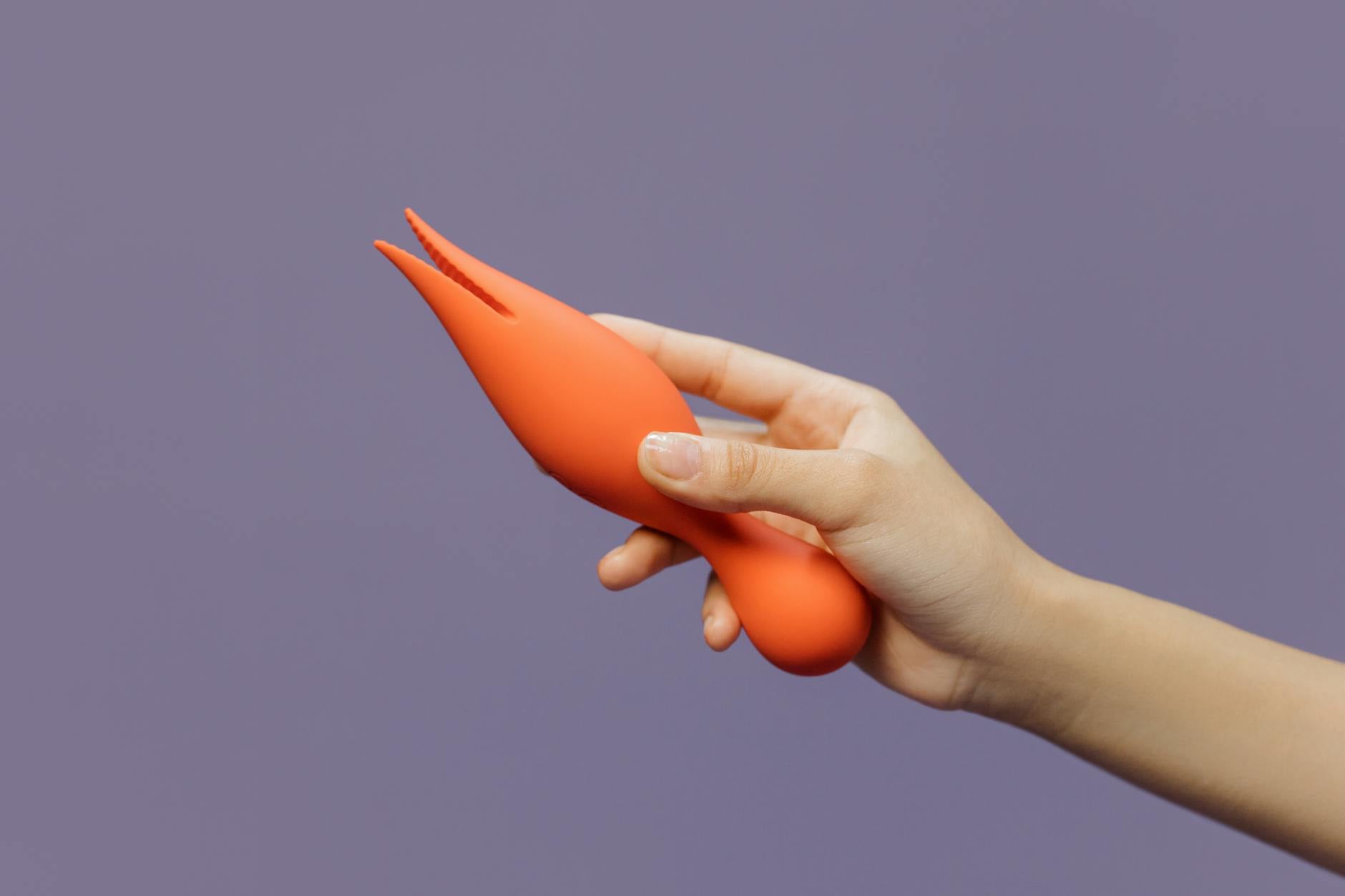 A hand holding a vibrant lemon-colored clitoral vibrator against a minimalist purple backdrop, symbolizing modern sensuality and self-care.
