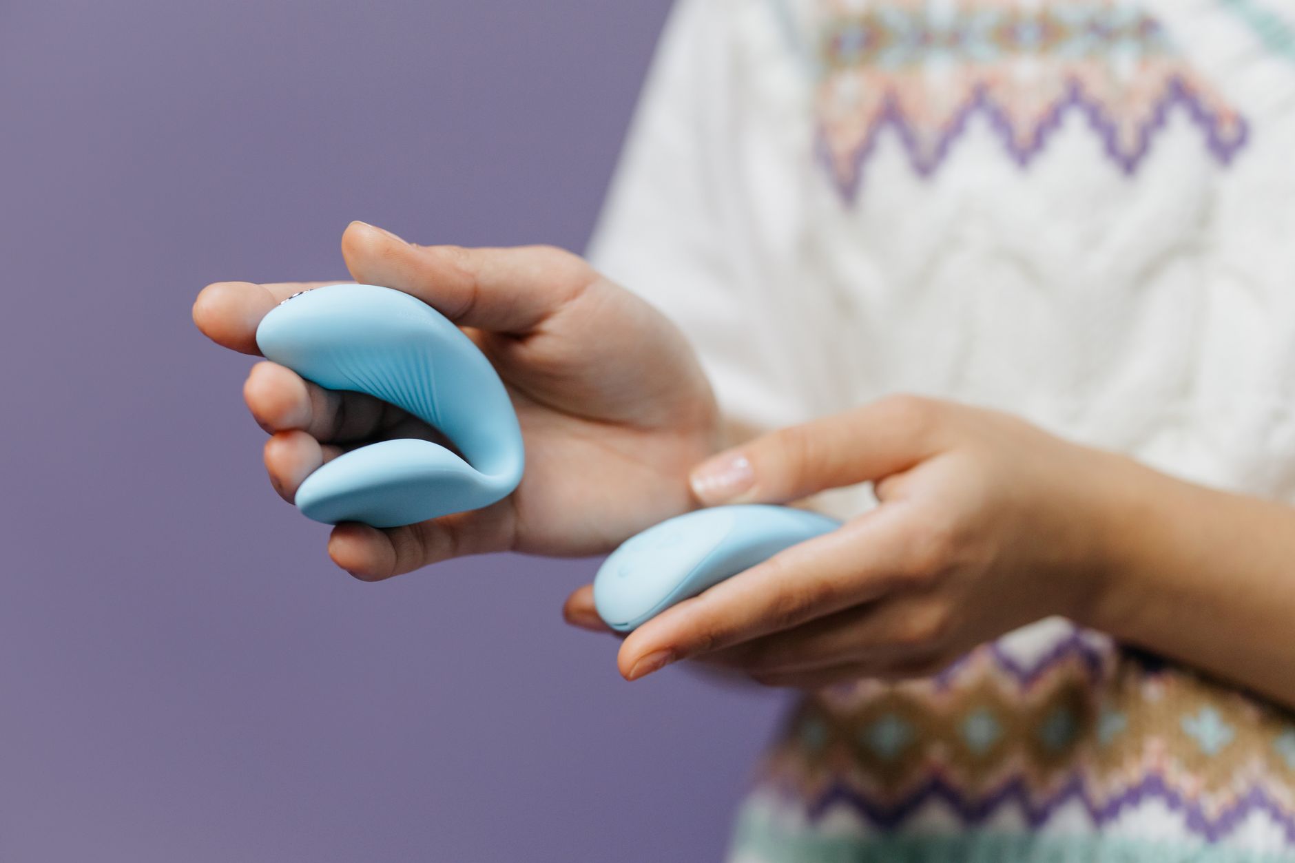 Detailaufnahme einer Hand, die einen eleganten blauen Vibrator hält, vor purpurnem Hintergrund
