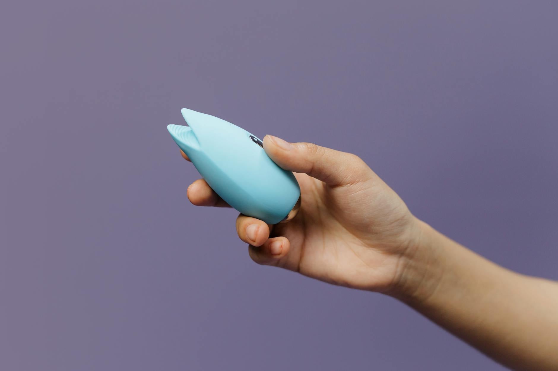 A blue silicone clitoral vibrator held in hand, representing modern pleasure tools for bodies on hormonal birth control.