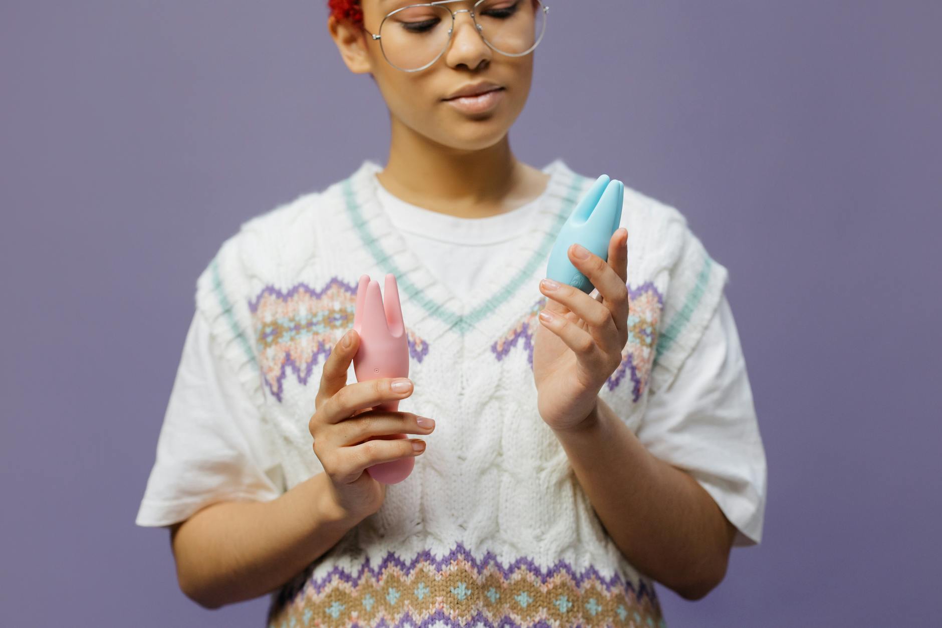 Woman holding blue and pink silicone vibrators in contemplative pose