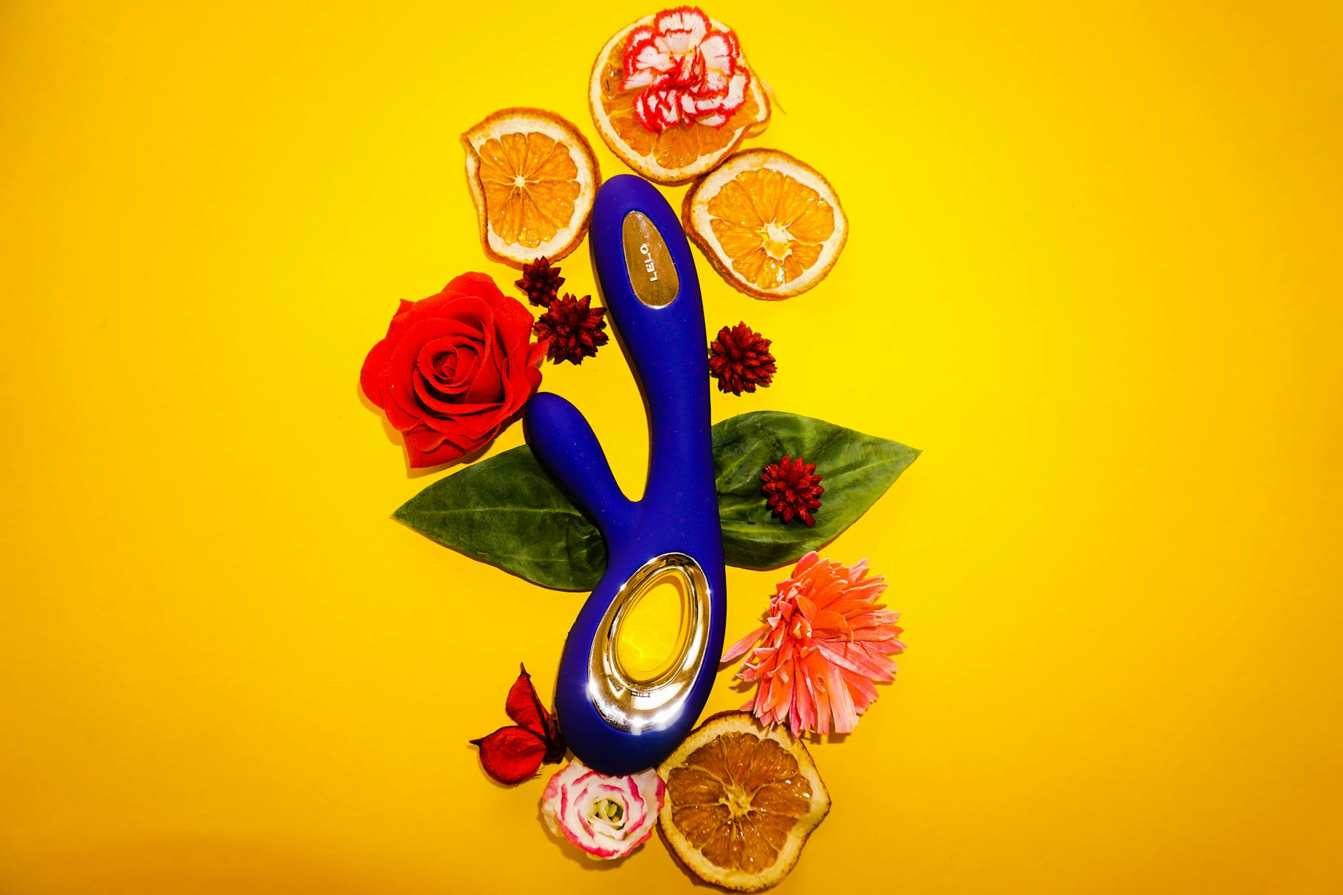 Ein blauer Lemon-Vibrator von oben, umgeben von Blumen und Zitronenscheiben auf gelbem Hintergrund